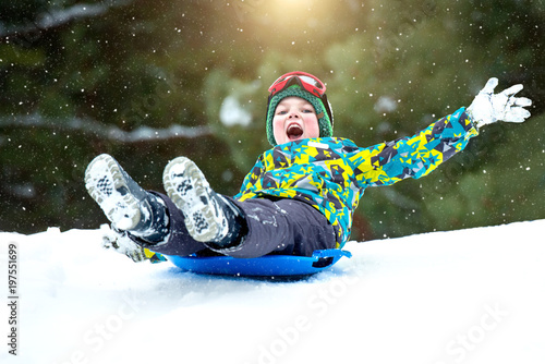  Boy sledding in a snowy forest. Outdoor winter fun for Christmas vacation. photo