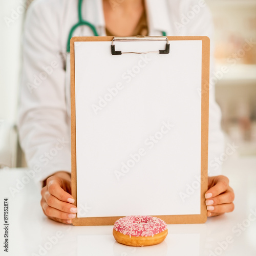 Closeup on doctor woman showing clipboard and donut
