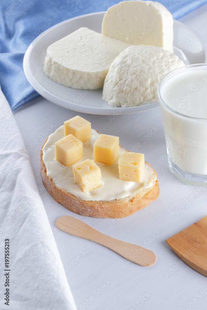 Cheese, dairy assortment on a white background, sandwich with soft cheese on a blue napkin, wooden background, wooden cutlery, top view, white cheese on a white plate, kefir in a glass, pop art