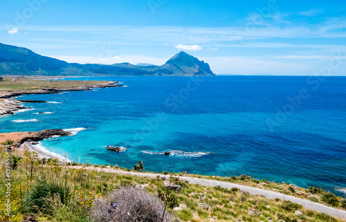 Panoramic road to drive over the Mediterranean sea. Wild coastline with rocks and sandy beaches, against a deep blue sea at San Vito Lo Capo, Palermo, Sicily. On the far background the Mount Cofano...