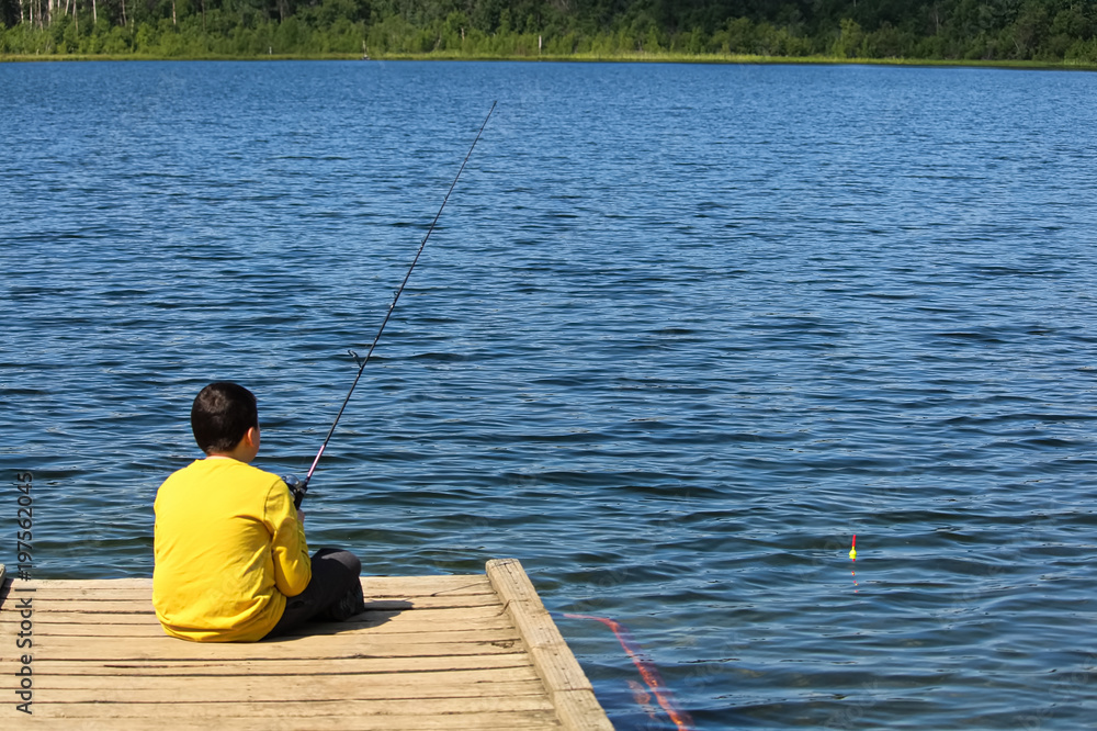 A young boy sitting on a dock and fishing A young boy sitting on a dock and fishing