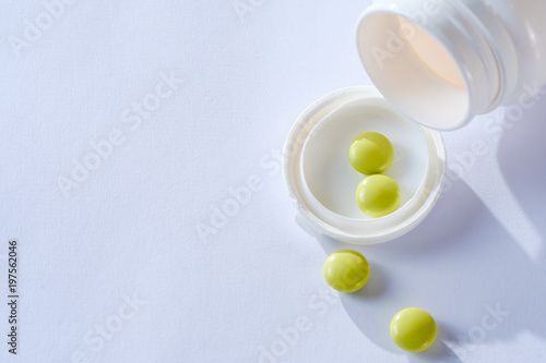 Heap of tablets medicine lying beside of plastic bottle. Pills and bottles are white. Isolated on white