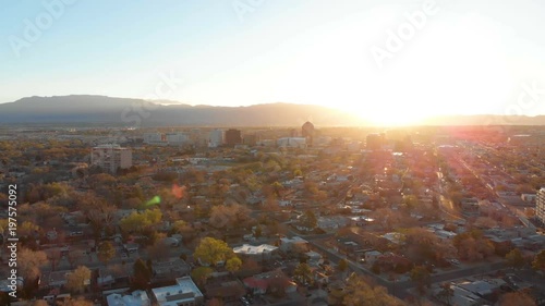 Cinematic aerial shot flying away from a city center with the sun rising over then mountains behind it