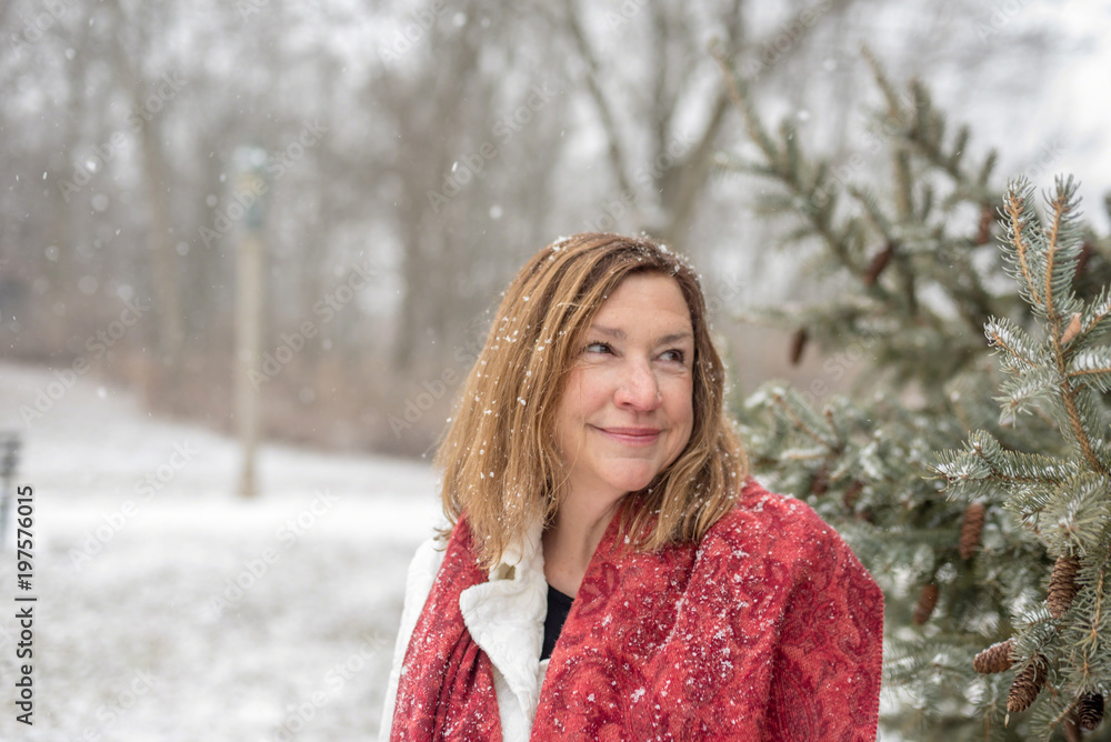 Smiling woman standing by pine tree outside in magical falling snow Smiling woman standing by pine tree outside in magical falling snow