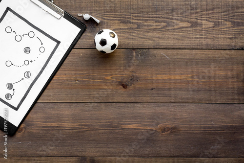 Sport coach concept. Pad with tactic plan of the match near whistle and football ball on wooden background top view copy space