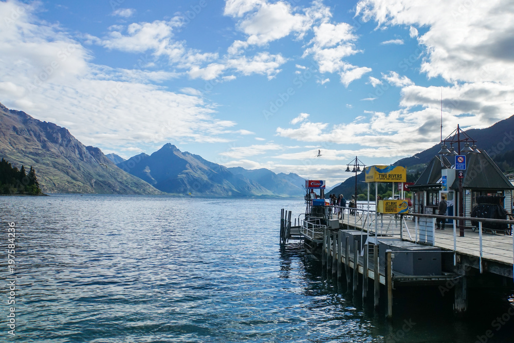 Queenstown / New Zealand - November 2 2017: Editorial wooden walkway to pier for passenger boat with mountain range in blue sky backdrop