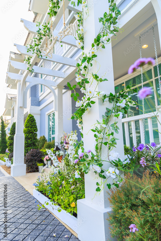 An artificial ivy with white flowers around the pillar with front yard background.