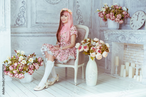 Photography Beautiful young woman doll in a pink dress in a room with flowers, sitting on a chair by the fireplace, lolita