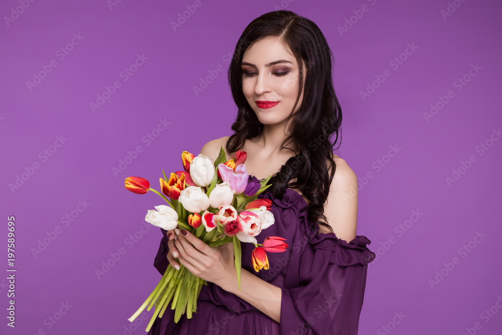 Beautiful young woman, brunette, stands on a purple background, in an air dress and a bouquet of tulips. International Women's Day, March 8. Beautiful young woman, brunette, stands on a purple background, in an air dress and a bouquet of tulips. International Women's Day, March 8.