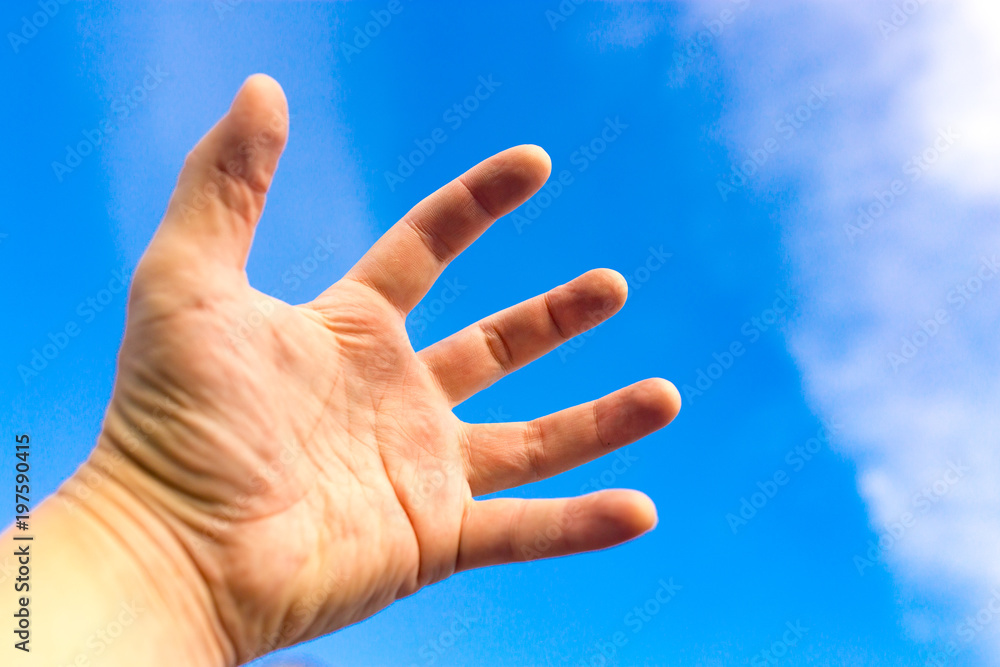 Male hand against a blue sky with clouds