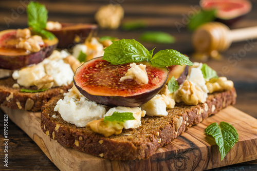 Healthy toasts with rye bread, fresh figs, honey, walnuts, mint leaves and cheese on the wooden board