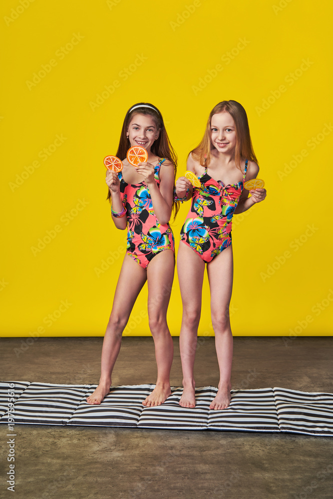 Girlfriends happy together,laughing summer day in swimsuit for beach,bikini.  Beautiful kids joy summertime,vacations,sun,recreation.Two teenager girls  on yellow background in studio,full length. foto de Stock | Adobe Stock