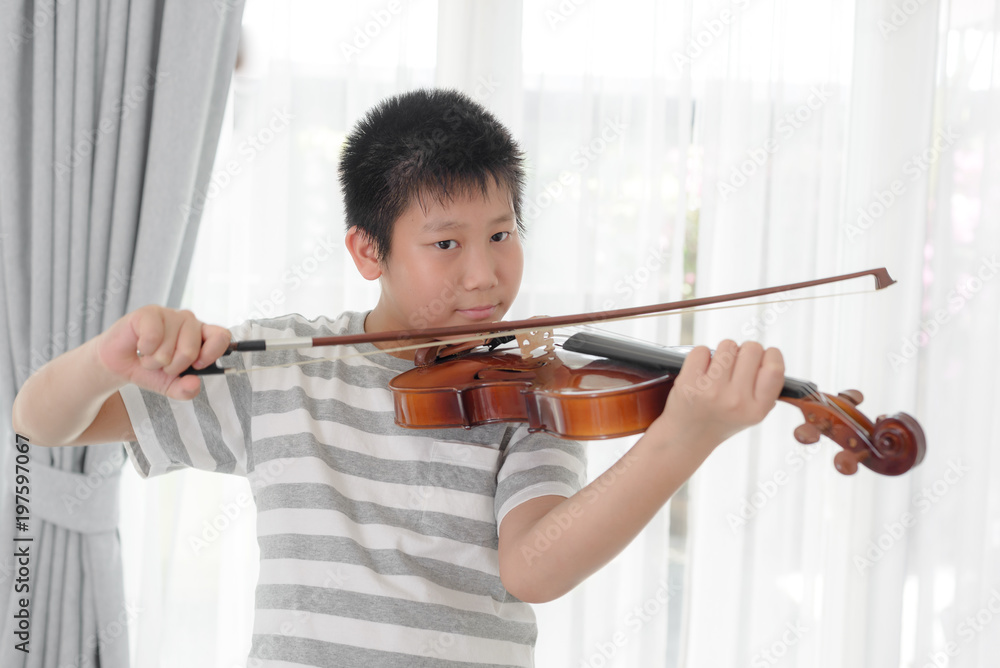 Happy Asian boy playing violin near window at home. Happy Asian boy playing violin near window at home.