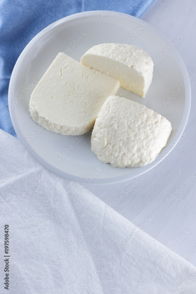 Cheese on a white background, soft cheese on a white plate, a glass of yogurt, minimalism, copy space, dairy products on a white blue napkin, French breakfast, American cuisine Cheese on a white background, soft cheese on a white plate, a glass of yogurt, minimalism, copy space, dairy products on a white blue napkin, French breakfast, American cuisine