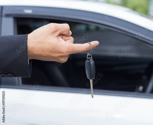 Male adult businessman in a suit  and holding a car key in his hand . White cars at the background © PRASERT
