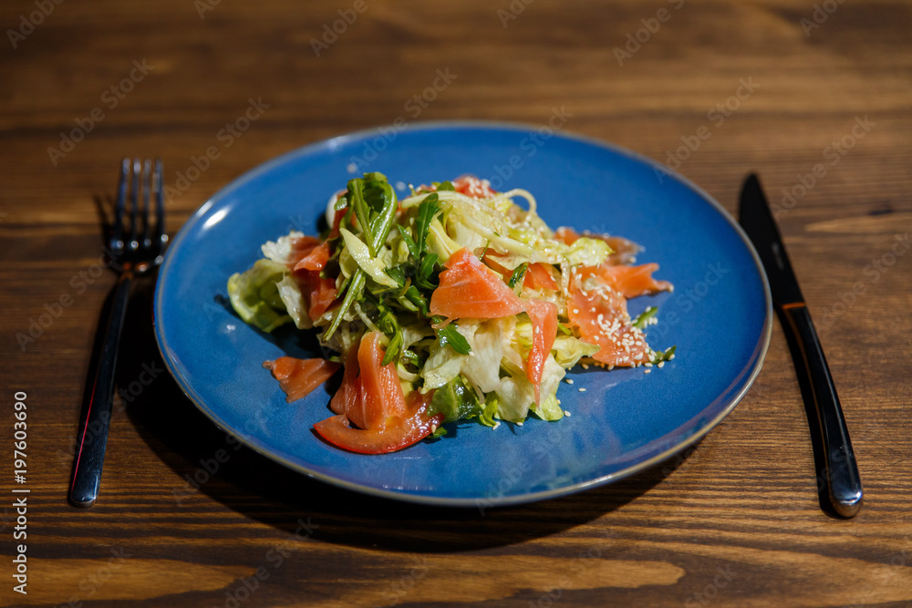 A horizontal image of a bright blue plate with salad, containing salmon, salad leaves, arugula, tomatoes, sesame seeds A horizontal image of a bright blue plate with salad, containing salmon, salad leaves, arugula, tomatoes, sesame seeds