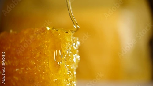 Honey dripping from honey dipper on honeycomb, over yellow background