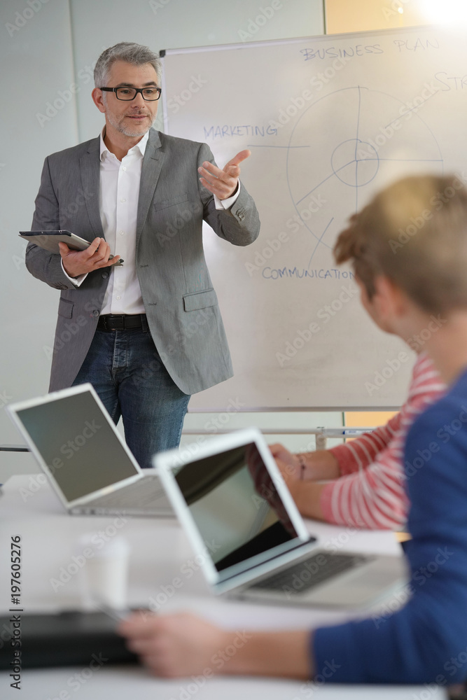 Teacher giving economics class, using whiteboard Teacher giving economics class, using whiteboard