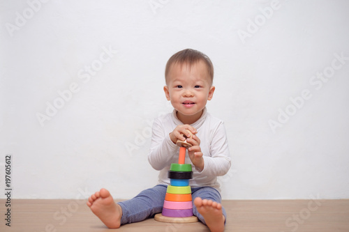Cute little Asian 18 months / 1 year old toddler baby boy child play with colorful wooden pyramid toy / stacking ring toy. Kid playing with educational toy isolated on white wall, with copy space