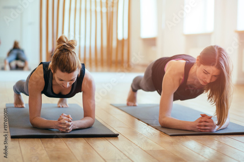 Carta da parati Front view of two sporty fit and slim middle aged women doing planking exercise indoors together with a natural light in modern interior sport studio hall or yoga class