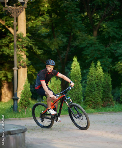 Sporty male cyclist in sportswear training on bike, riding paved park alley. Muscle sportsman getting ready for contest. Concept of healthy lifestyle