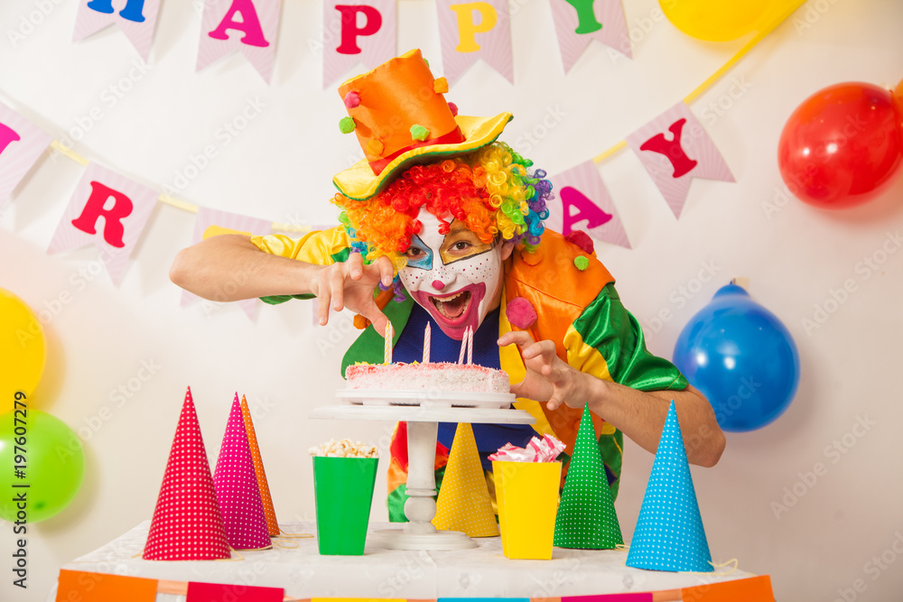 Clowns are a boy in bright costumes at the child's birthday. A table with refreshments and a cake. The explosion of emotions and the fun of the circus. greed and desire to eat cake