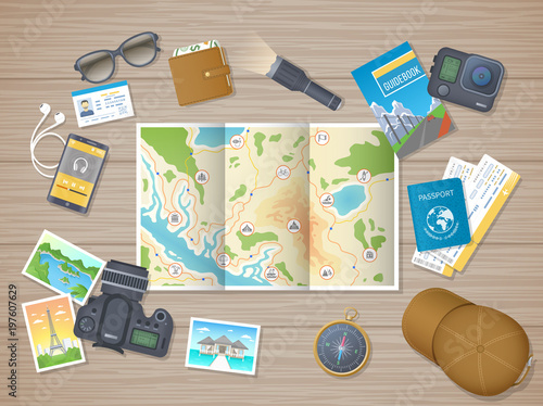 Preparing for hiking tour, vacation, travel. Planning, packing check list. Wooden table with tourist map, guidebook, tickets, passport, flashlight, action camera, compass, cap. Wooden table top view