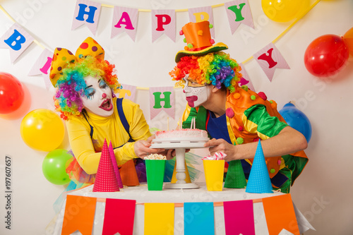 Clowns are a boy and a girl in bright costumes at the child's birthday. A table with refreshments and a cake. The explosion of emotions and the fun of the circus. greed and desire to eat cake