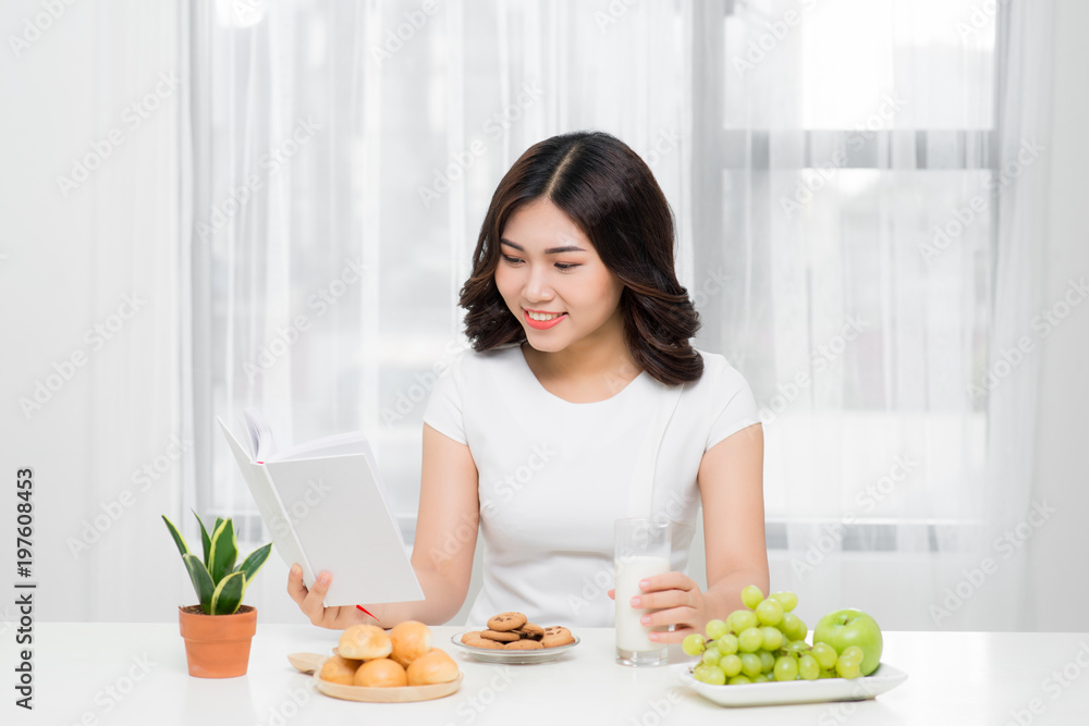 Smiling happy woman having a relaxing healthy breakfast at home sitting at kitchen table, she is reading book