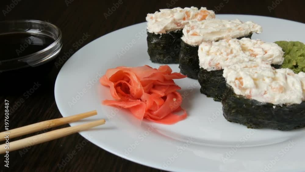 A large white plate on which lies four huge sushi nigiri next to pink ginger and green wasabi A large white plate on which lies four huge sushi nigiri next to pink ginger and green wasabi