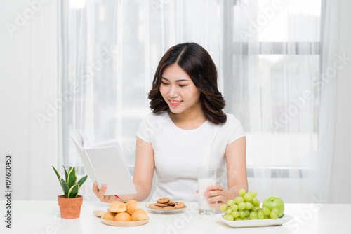 Smiling happy woman having a relaxing healthy breakfast at home sitting at kitchen table  she is reading book
