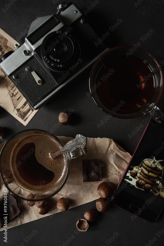 Two transparent cups of coffee, hazelnut, film camera and retro cards on a dark grunge background. The concept. Vintage. Flat lay. Toned