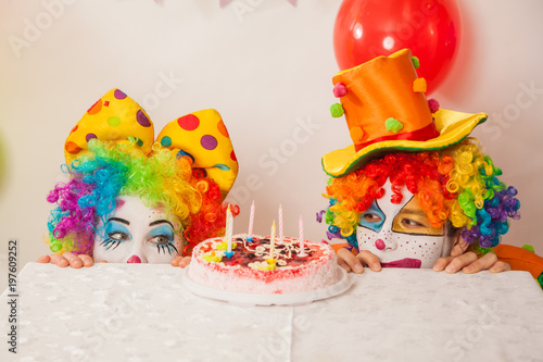 Clowns are a boy and a girl in bright costumes at the child's birthday. A table with refreshments and a cake. The explosion of emotions and the fun of the circus. greed and desire to eat cake © izida1991