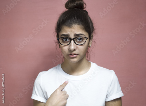 You to me  Who am I  Portrait of a beautiful Indian girl in a white T-shirt and glasses  questioningly points at herself  an indeterminate facial expression. 