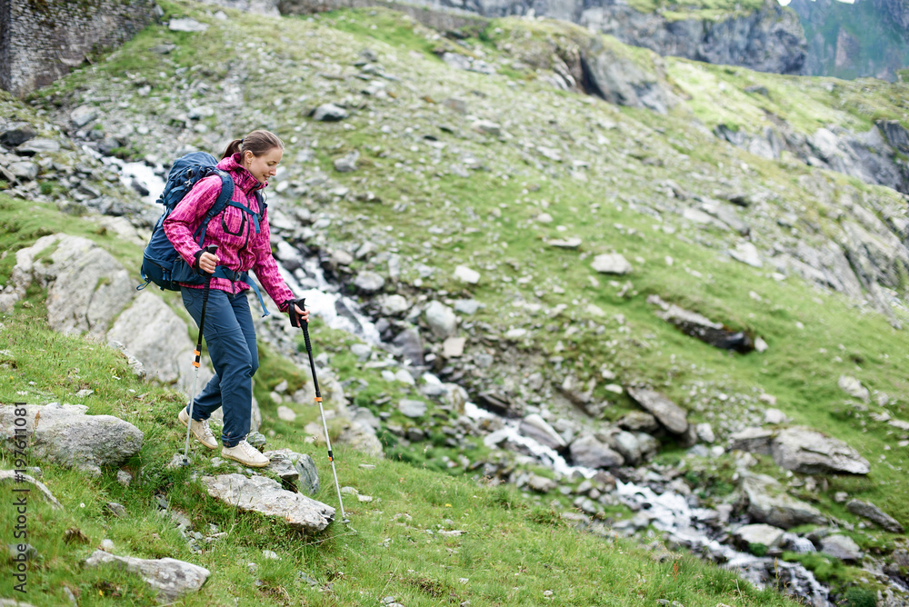 Young female climber hiking in the mountains with her backpack and trekking poles copyspace exploring nature lifestyle tourism recreation concept