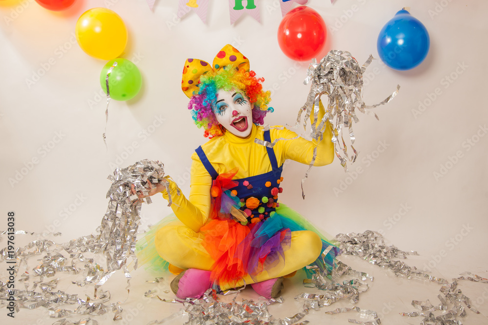 Fototapeta premium A clown girl in a bright suit at the baby's birthday party. The explosion of emotions and the fun of the circus. Paper disco made of silver paper
