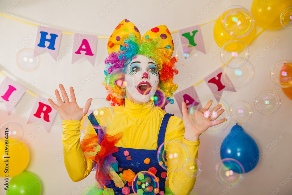 A clown girl in a bright suit at the baby's birthday party. The explosion of emotions and the fun of the circus. The sea of soap bubbles A clown girl in a bright suit at the baby's birthday party. The explosion of emotions and the fun of the circus. The sea of soap bubbles