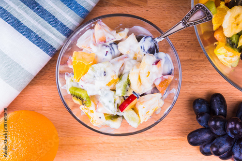 Delicious fruit salad with yogurt in a glass cup on a wooden table - top view, fruit diet