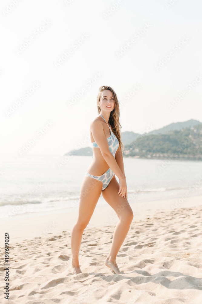 slim woman posing on sandy beach at the ocean