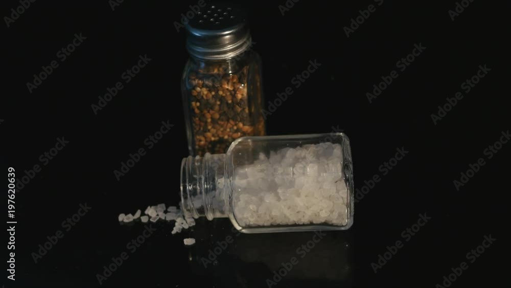 Sea Salt and Black Pepper displayed in glass Jars on black backgound Sea Salt and Black Pepper displayed in glass Jars on black backgound