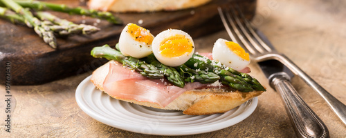 Fresh sendwich with ham, asparagus and quail eggs on old wooden chopping board. Easter spring breakfast concept with copy space. Banner.