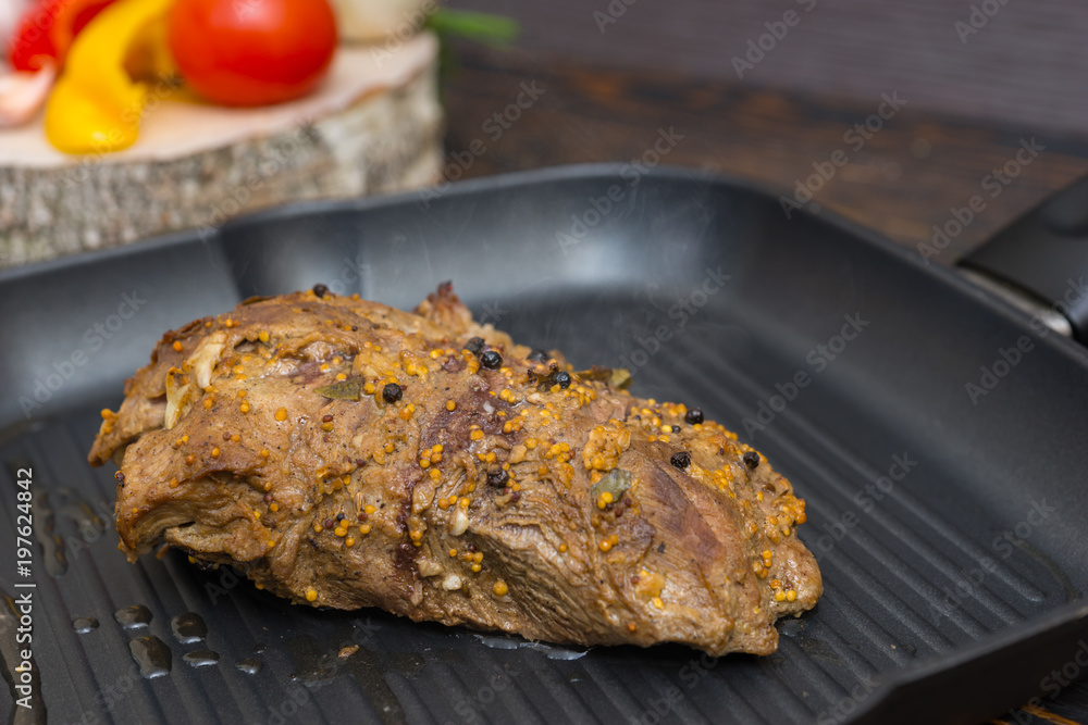 Close up of prepared meat on a grill pan next to vegetables on wooden desk