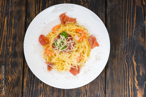 High angle view of tasty spaghetti pasta with shrimps, grated cheese, jamon, tomato sauce and basil in white plate