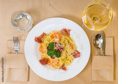 High angle view of spaghetti pasta in white plate near glass with wine and a glass for water on decorated table with light tablecloth