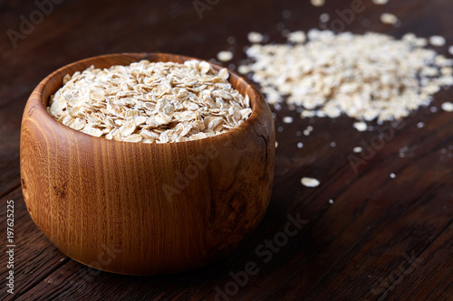 Oat flakes in bowl and wooden spoon isolated on wooden background, close-up, top view, selective focus. photo