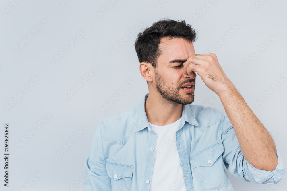 Studio horizontal portrait of male has headache massaging nose bridge to release tension after long working, isolated on white studio background with copy space.Stress, people, health, emotion concept Studio horizontal portrait of male has headache massaging nose bridge to release tension after long working, isolated on white studio background with copy space.Stress, people, health, emotion concept
