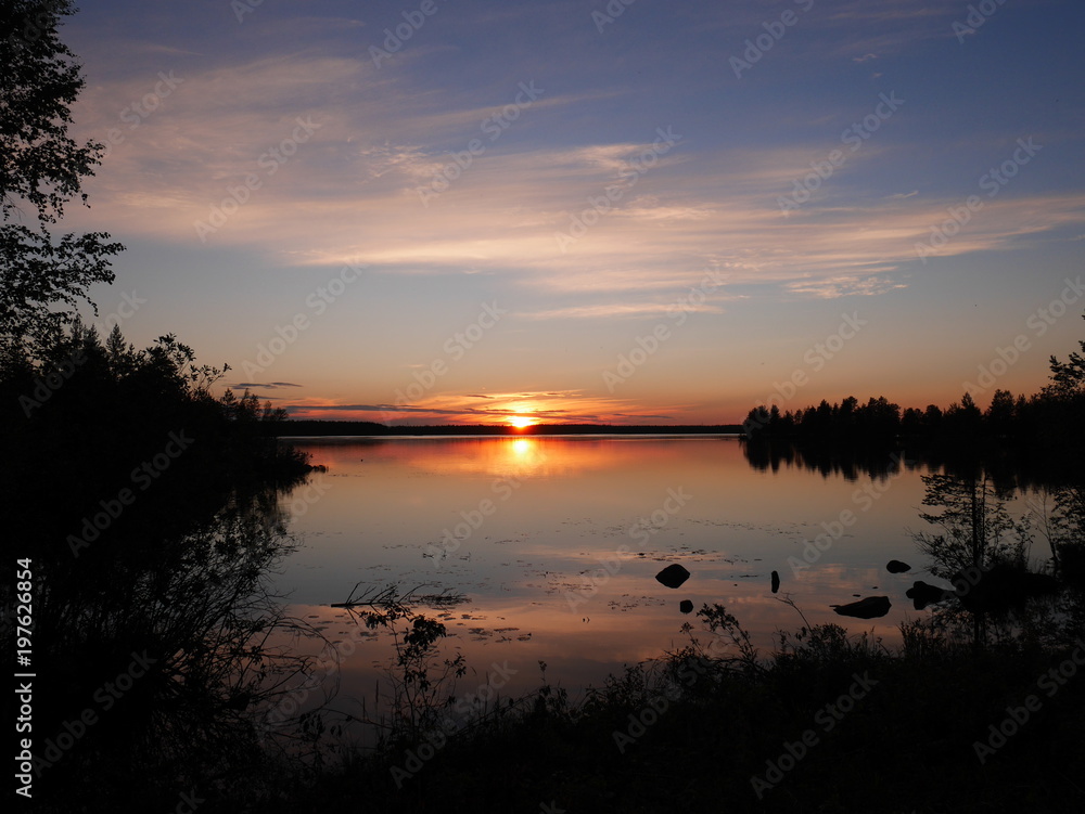 Karelia sunset with dark black silhouettes of forest with a clear reflection in water 