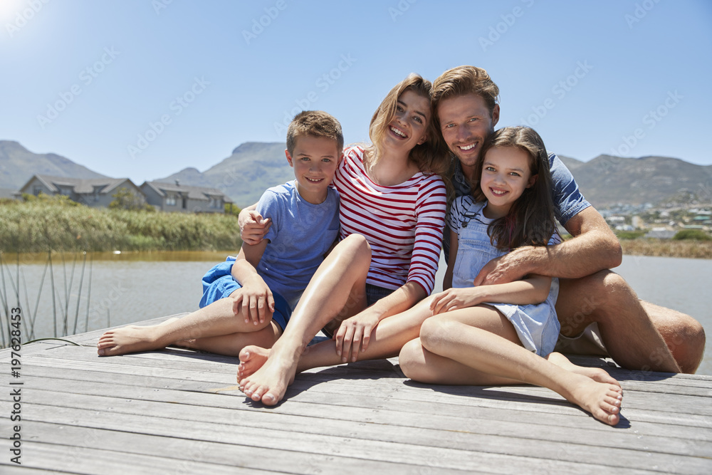 Portrait Of Smiling Family Sitting On Wooden Jetty By Lake Portrait Of Smiling Family Sitting On Wooden Jetty By Lake