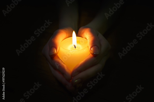 burning candle in the hands of a praying girl on a black background