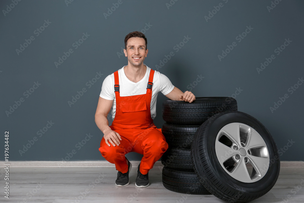Young mechanic in uniform with car tires near dark wall Young mechanic in uniform with car tires near dark wall